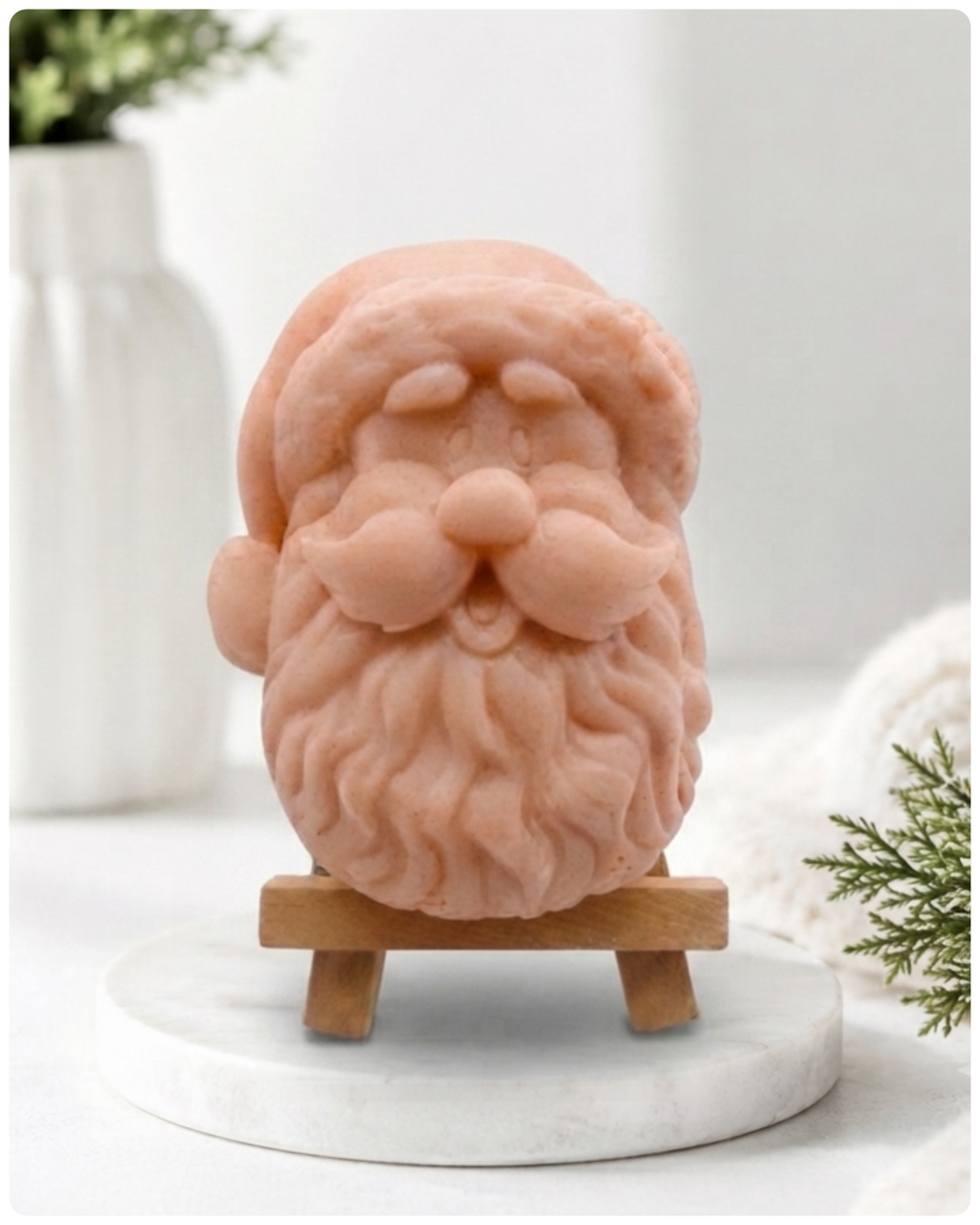 handmade vegan soap sculpted in the shape of Father Christmas's head, featuring a detailed curly beard, a jolly moustache, and a classic Santa hat, displayed on a miniature wooden easel in a bright farmhouse setting.