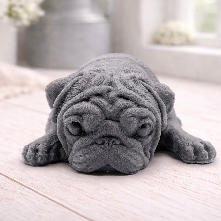 A detailed handmade vegan soap gift, sculpted in the shape of a pug dog lying flat on its stomach in a sleeping position, showing realistic skin folds and fur texture
