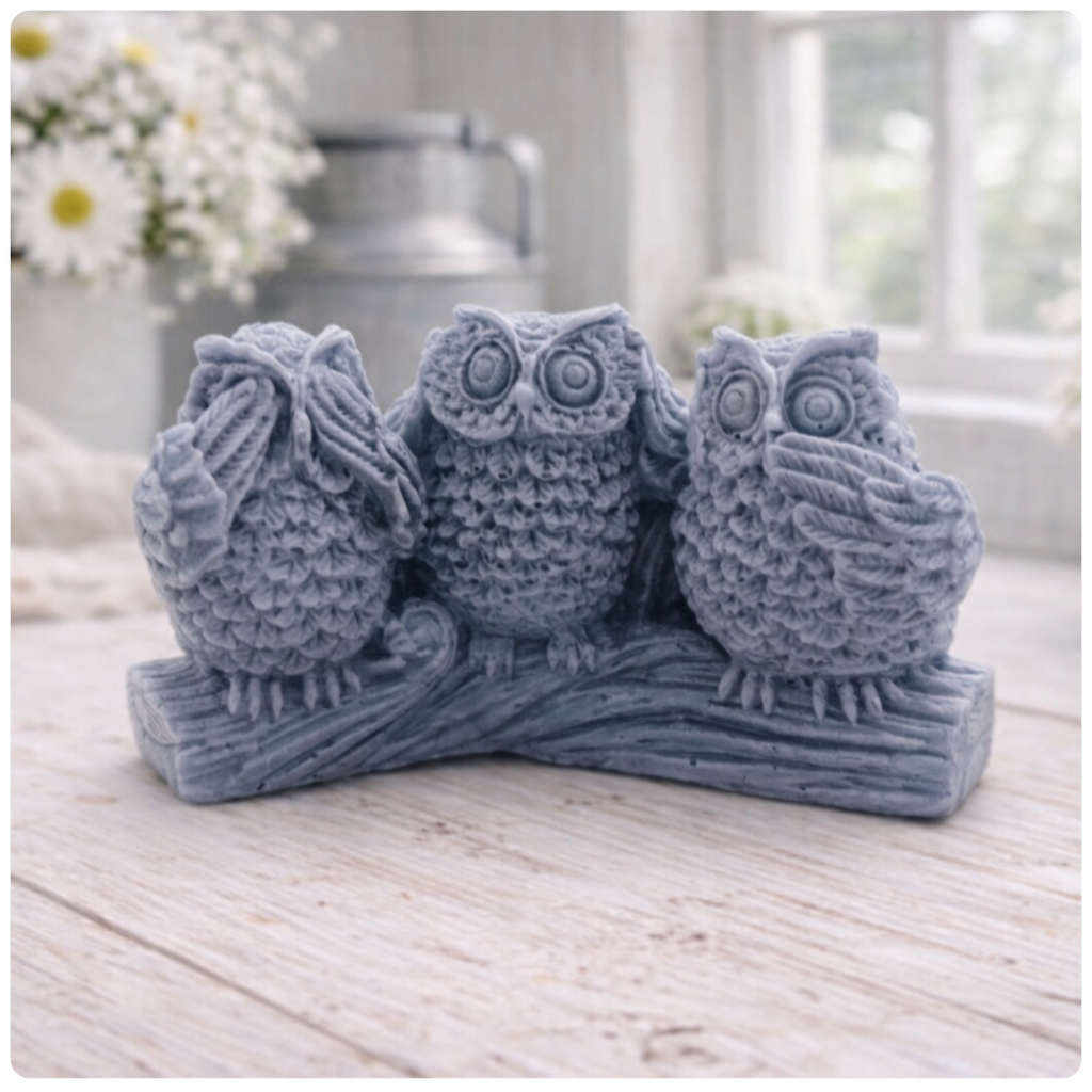 A handmade vegan soap gift featuring three owls perched on a branch in the "See No Evil, Hear No Evil, Speak No Evil" poses, set against a bright window with white flowers.