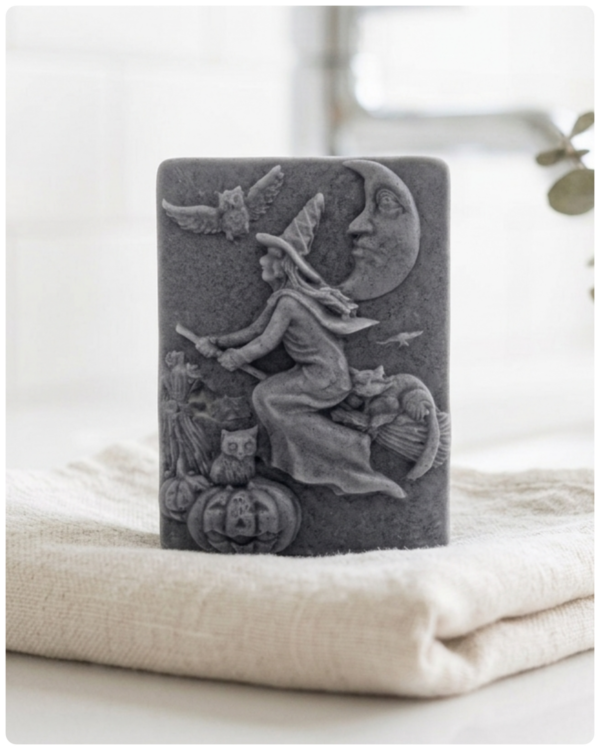handmade vegan soap bar featuring a detailed relief carving of a witch flying on a broomstick past a crescent moon, owls, and pumpkins.