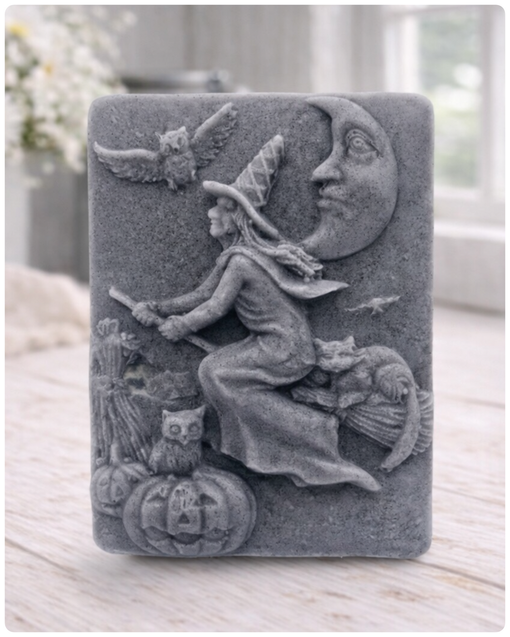 handmade vegan soap bar featuring a detailed relief carving of a witch flying on a broomstick past a crescent moon, owls, and pumpkins.