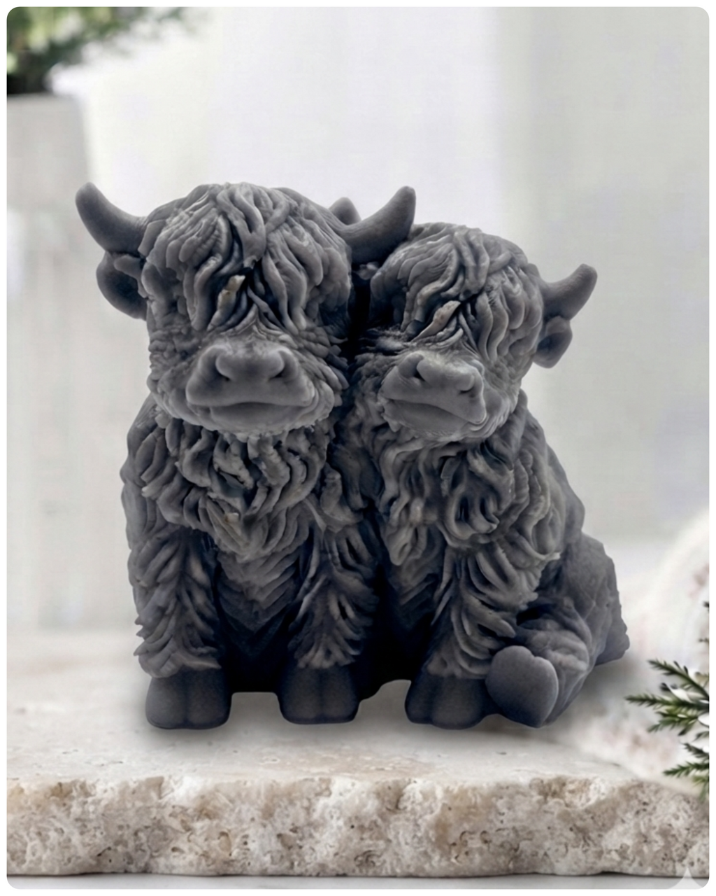 Handmade soap featuring two Highland cows with textured, shaggy fur sitting side by side on a light wooden surface with a softly indoor background.