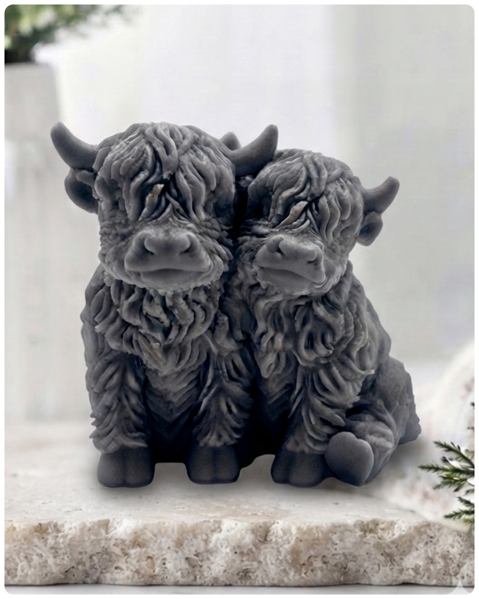 Handmade soap featuring two Highland cows with textured, shaggy fur sitting side by side on a light wooden surface with a softly indoor background.