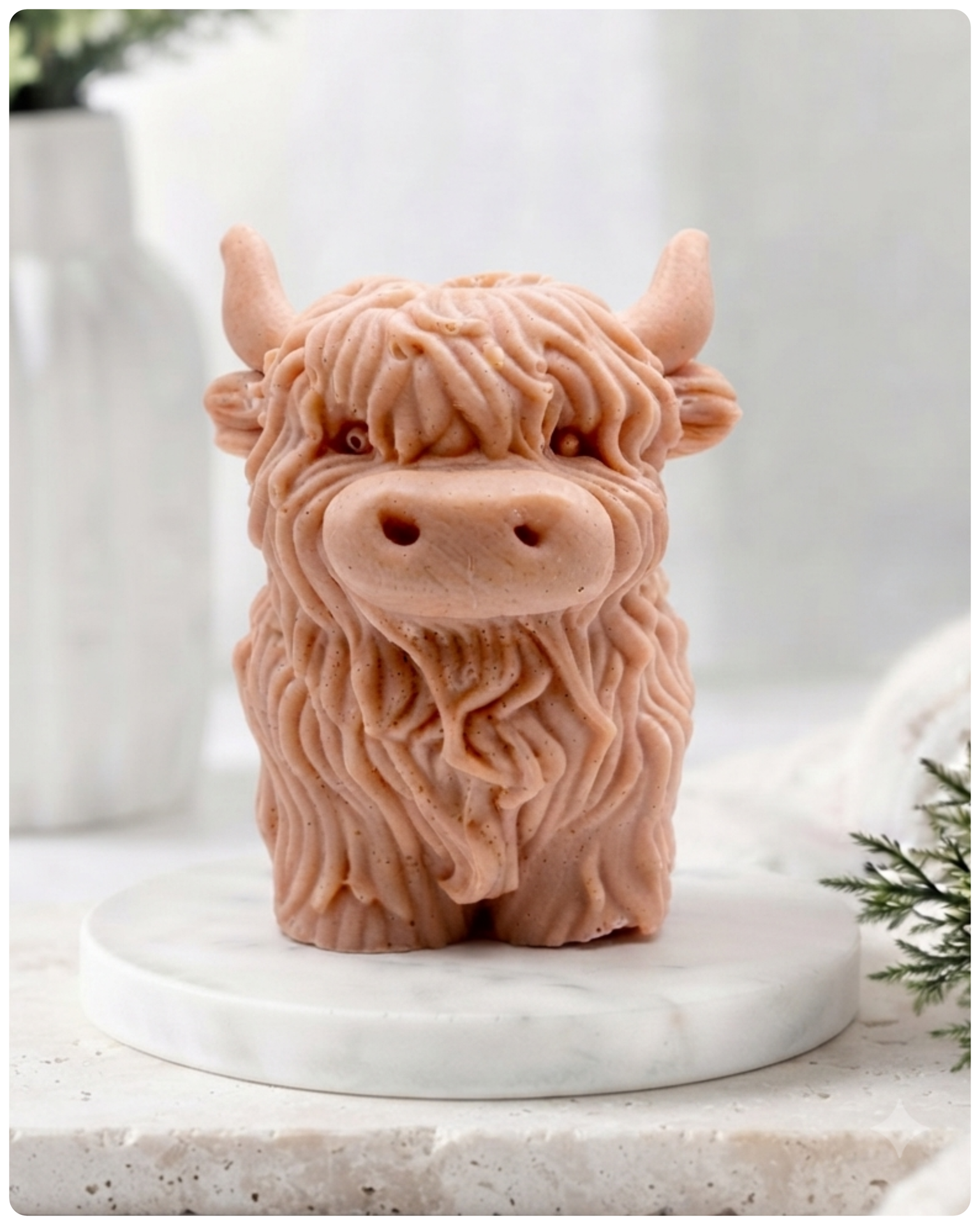 A detailed handmade vegan soap in a warm terracotta hue, sculpted in the shape of a highland cow with characteristic long, wavy fur, horns, and a friendly face, displayed on a light wooden surface.
