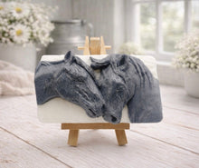 Load image into Gallery viewer, A rectangular handmade vegan soap featuring a detailed relief of two horse heads leaning affectionately towards each other, finished in a slate-grey tone against a white soap base and displayed on a miniature wooden easel.
