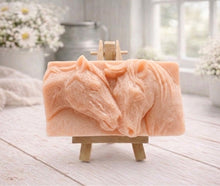 Load image into Gallery viewer, A rectangular handmade vegan soap featuring a detailed relief of two horse heads leaning affectionately towards each other, finished in soft natural tones and displayed on a miniature wooden easel.
