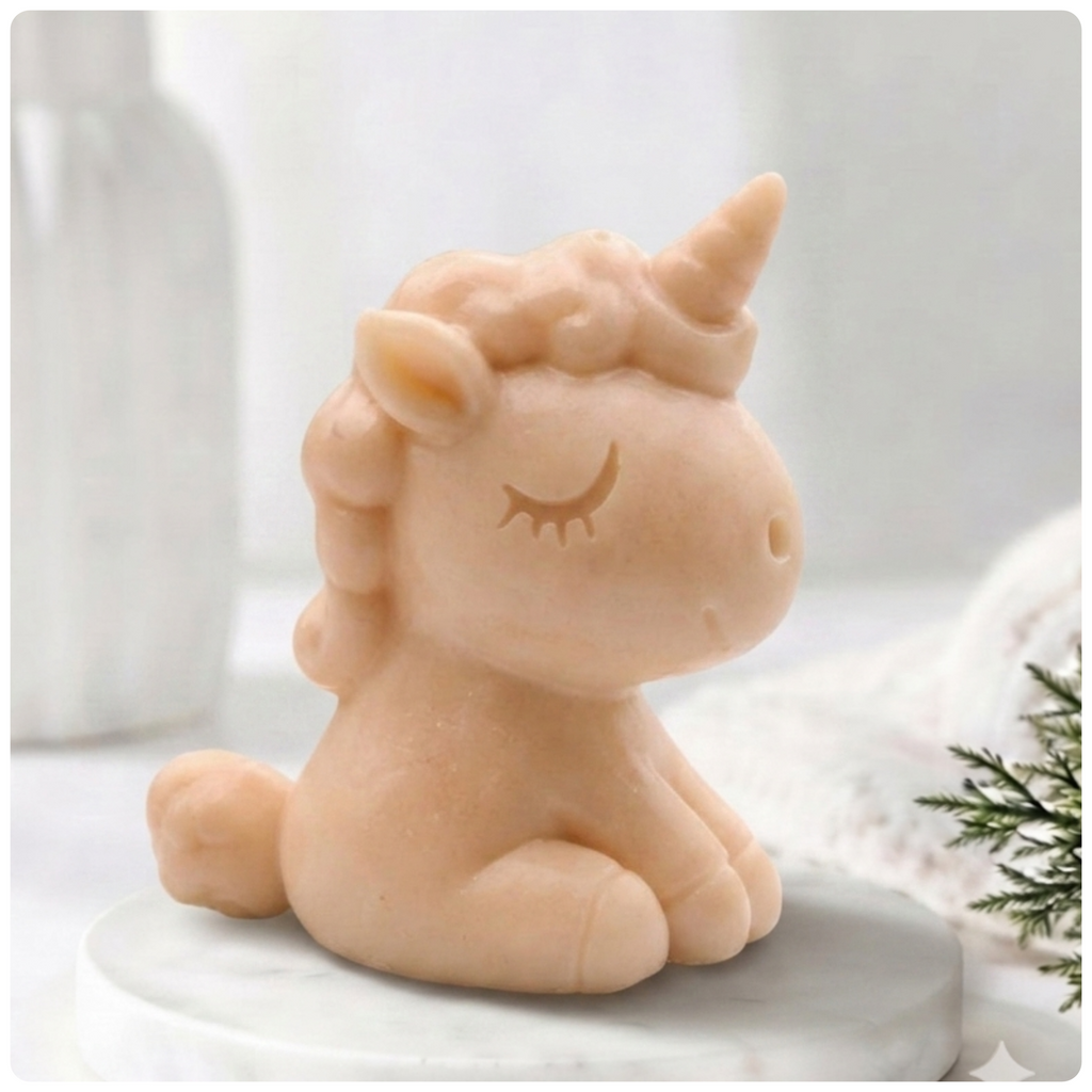A pink unicorn soap figurine with closed eyes and a horn, sitting on a round white surface against a softly blurred light background.