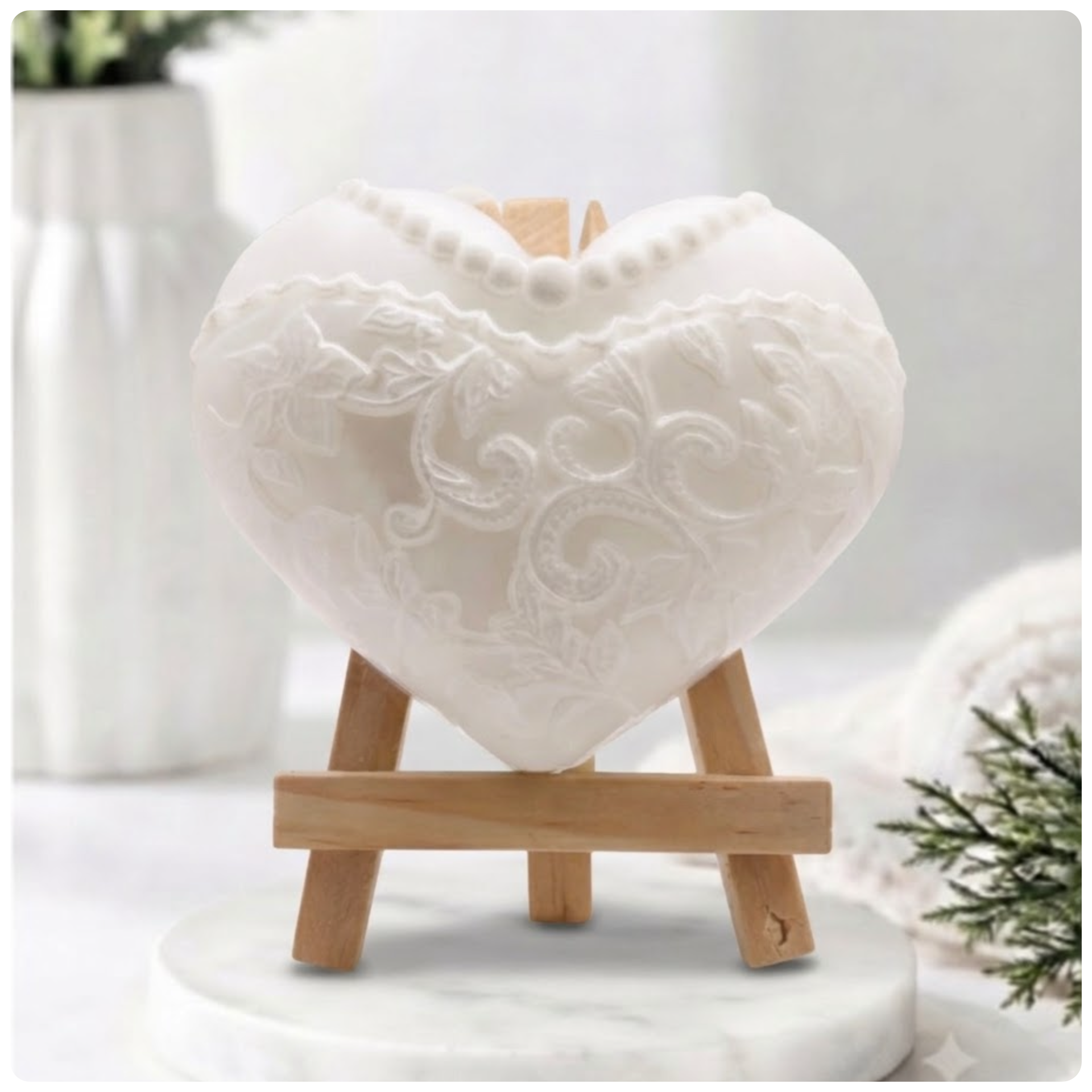 White heart-shaped artisan soap sculpted with detailed floral lace embroidery and a pearl necklace pattern, displayed on a wooden mini easel.