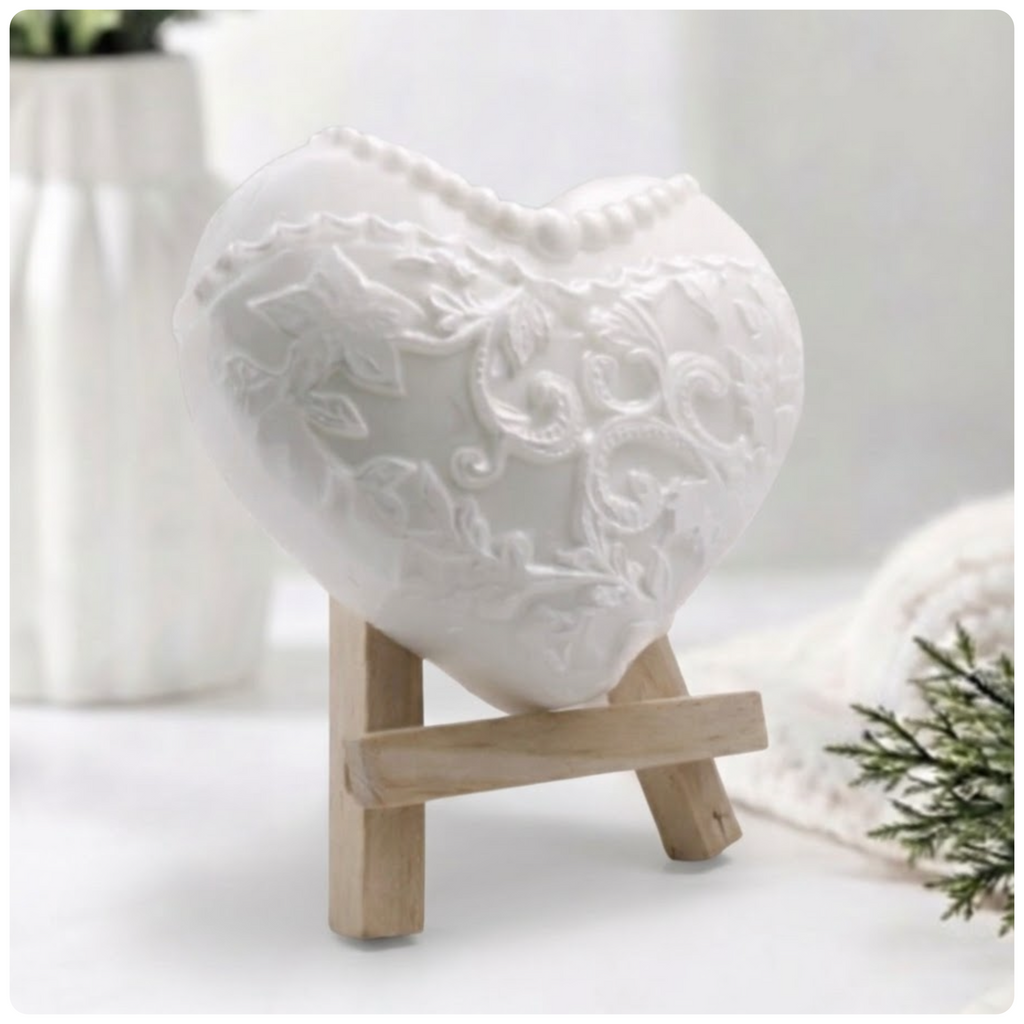 White heart-shaped artisan soap sculpted with detailed floral lace embroidery and a pearl necklace pattern, displayed on a wooden mini easel.