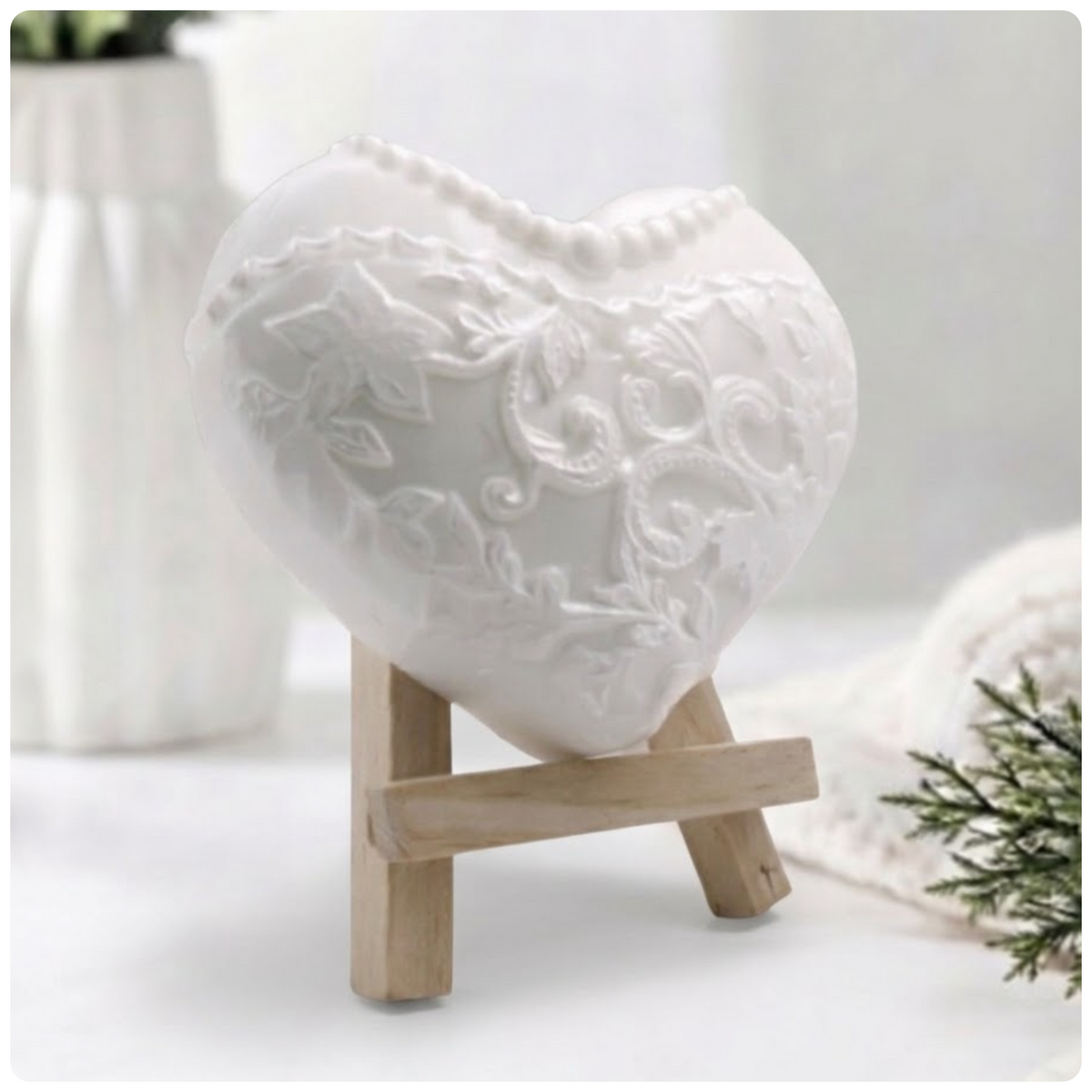 White heart-shaped artisan soap sculpted with detailed floral lace embroidery and a pearl necklace pattern, displayed on a wooden mini easel.