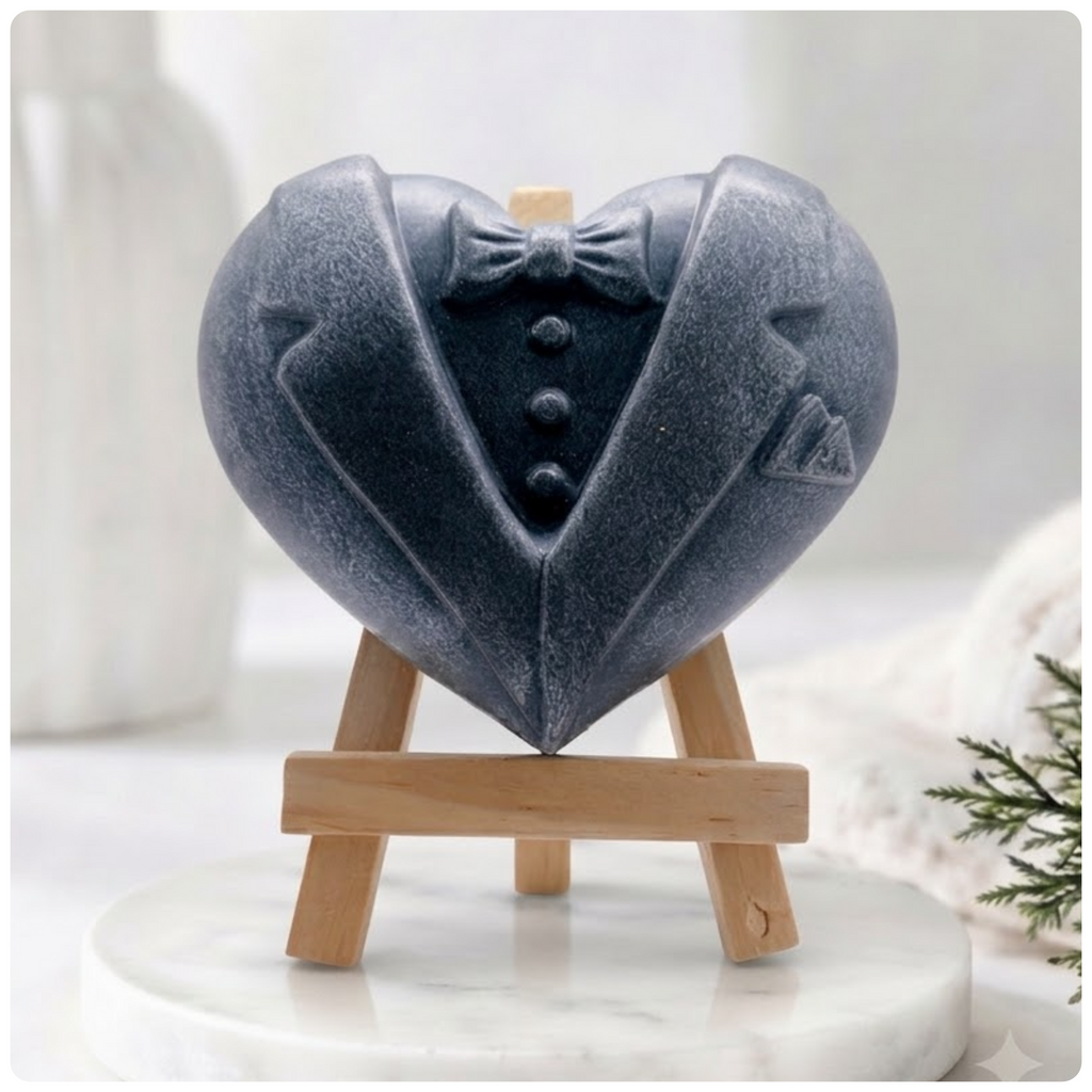Charcoal grey heart-shaped soap bar carved to resemble a dapper tuxedo suit with lapels, a bow tie, buttons, and a pocket square, sitting on a mini easel.