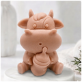 A baby cow-shaped soap holding a small milk bottle, photographed on a soft white background with a blurred bottle and greenery in the surroundings.