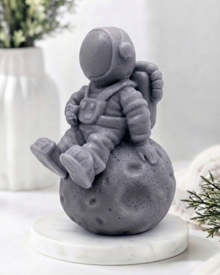 handmade vegan soap in the shape of a realistic astronaut sculpture sitting on the moon, featuring detailed spacesuit textures and craters on the lunar surface, displayed in a bright farmhouse decor setting.