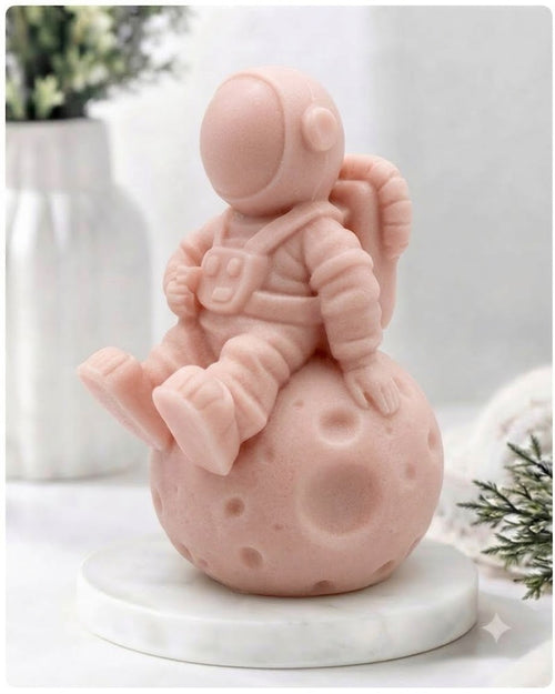 handmade vegan soap in the shape of a realistic astronaut sculpture sitting on the moon, featuring detailed spacesuit textures and craters on the lunar surface, displayed in a bright farmhouse decor setting.