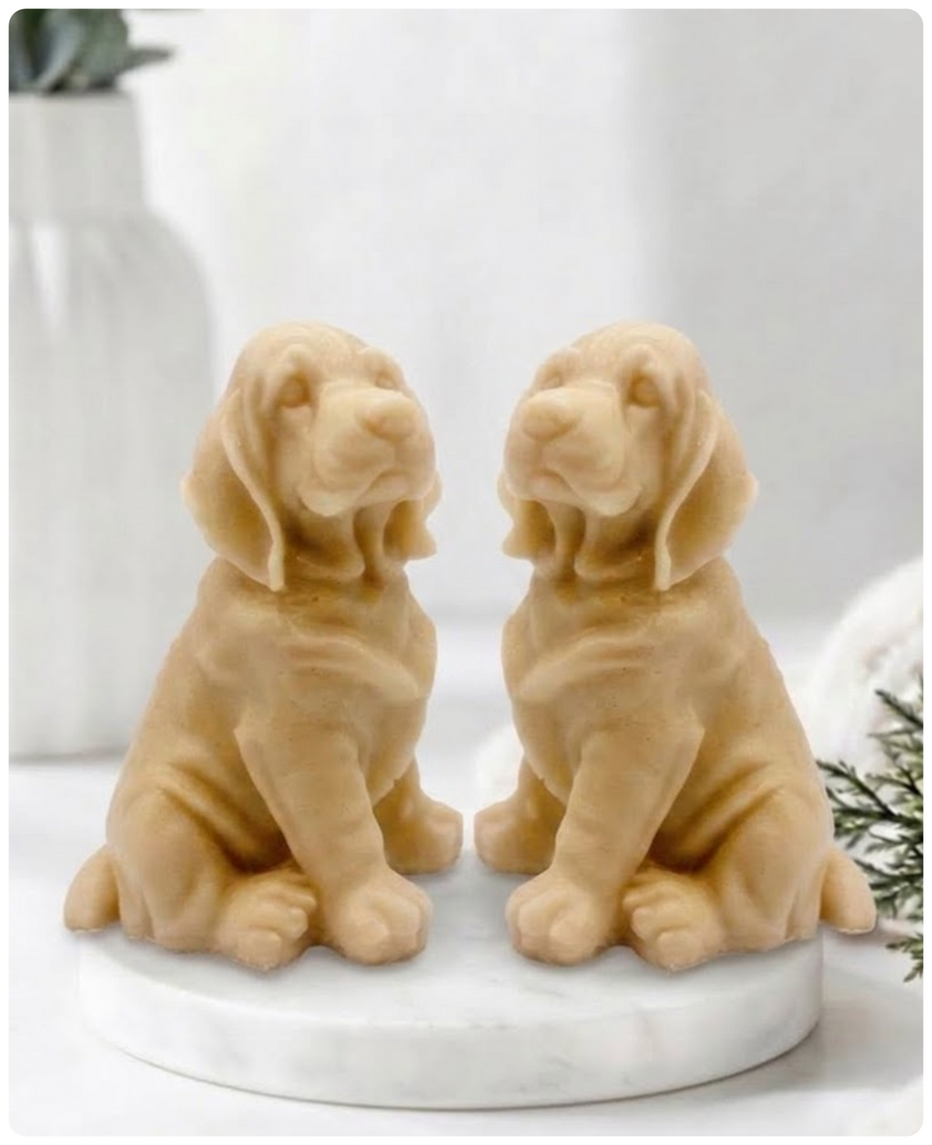 Two yellow Golden Retriever soap sitting on a white marble display stand with a soft bathroom background.