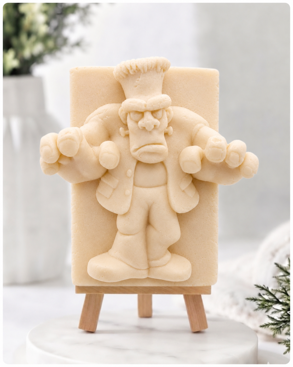 A rectangular handmade vegan soap featuring a high-relief carving of Frankenstein's monster in a classic pose with arms outstretched and a grumpy expression, displayed on a miniature wooden easel.