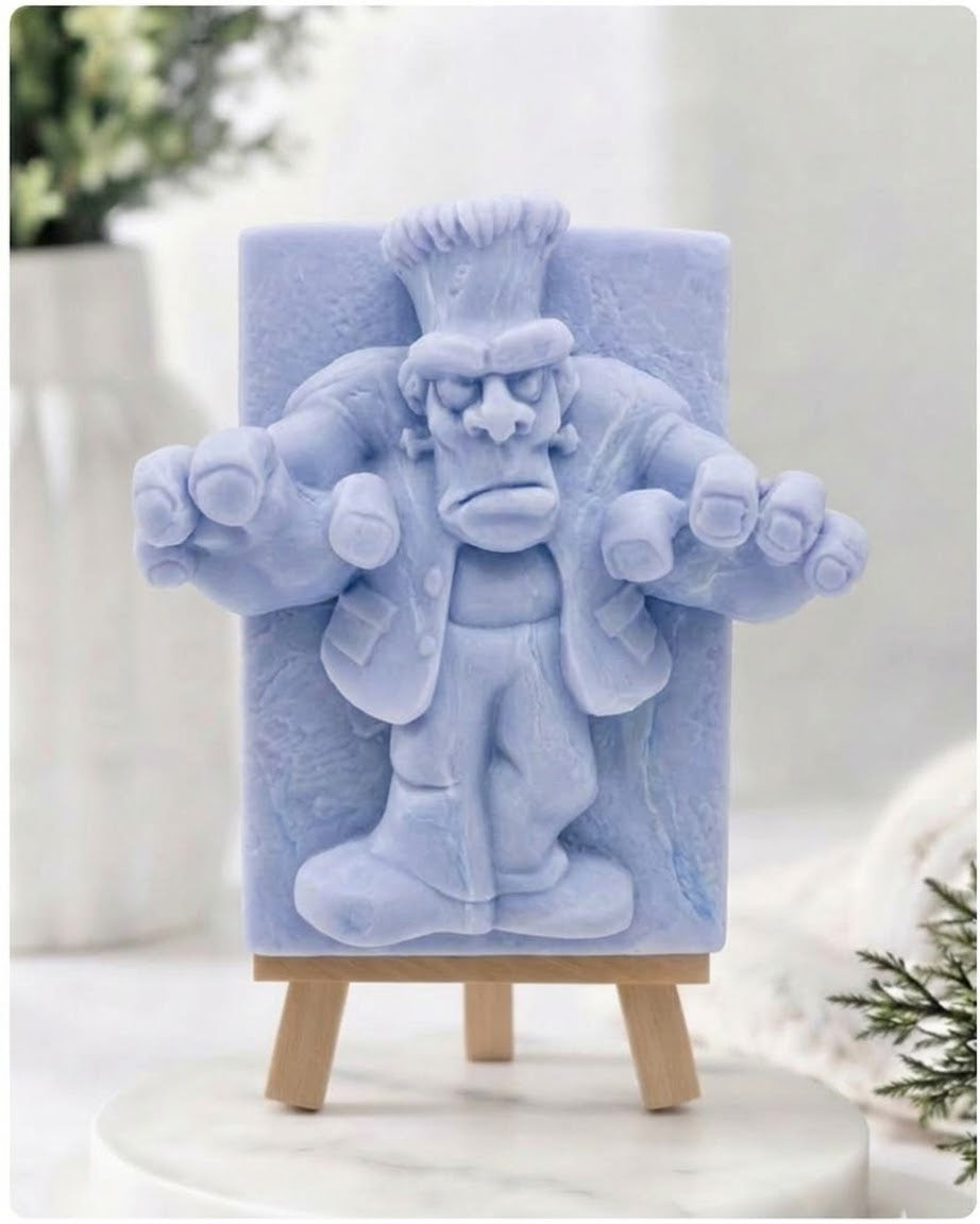 A rectangular handmade vegan soap featuring a high-relief carving of Frankenstein's monster in a classic pose with arms outstretched and a grumpy expression, displayed on a miniature wooden easel.