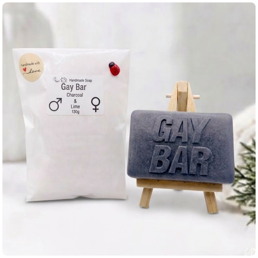 A rectangular handmade vegan soap featuring the words "GAY BAR" in large, bold, 3D block lettering, displayed on a miniature wooden easel.