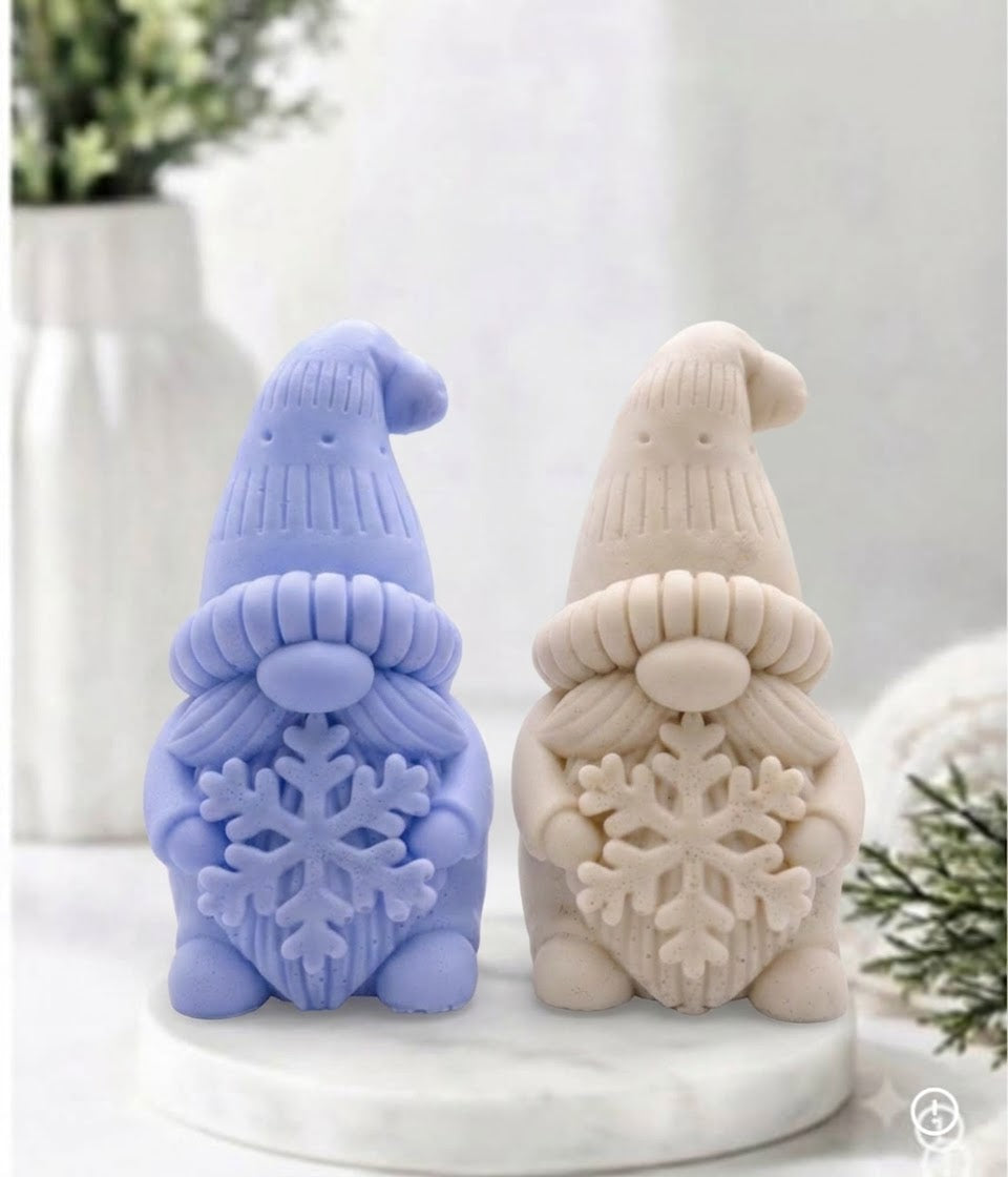 Two handmade vegan soaps in the shape of a winter gnome sculpture holding a large snowflake, featuring a tall textured hat and a bushy moustache 