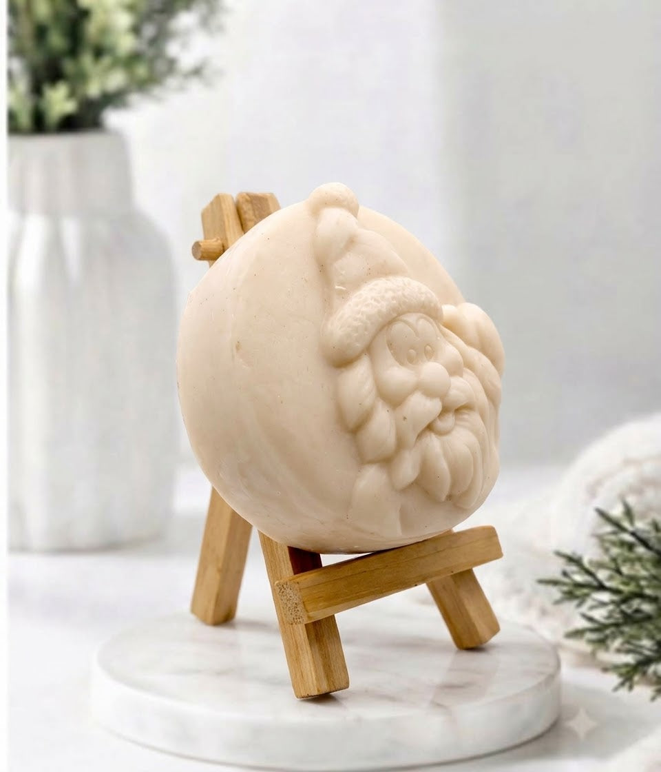 A round, yellow soap or candle featuring a relief carving of Santa Claus's face, displayed on a small wooden easel stand over a white marble base.