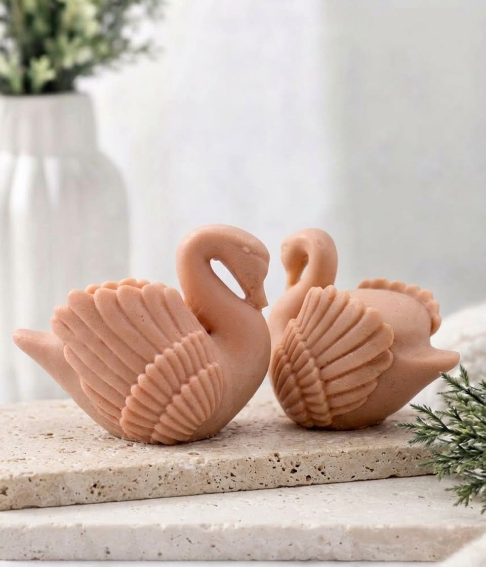 A pair of handmade swan soap bars resting together on a textured slab dish.