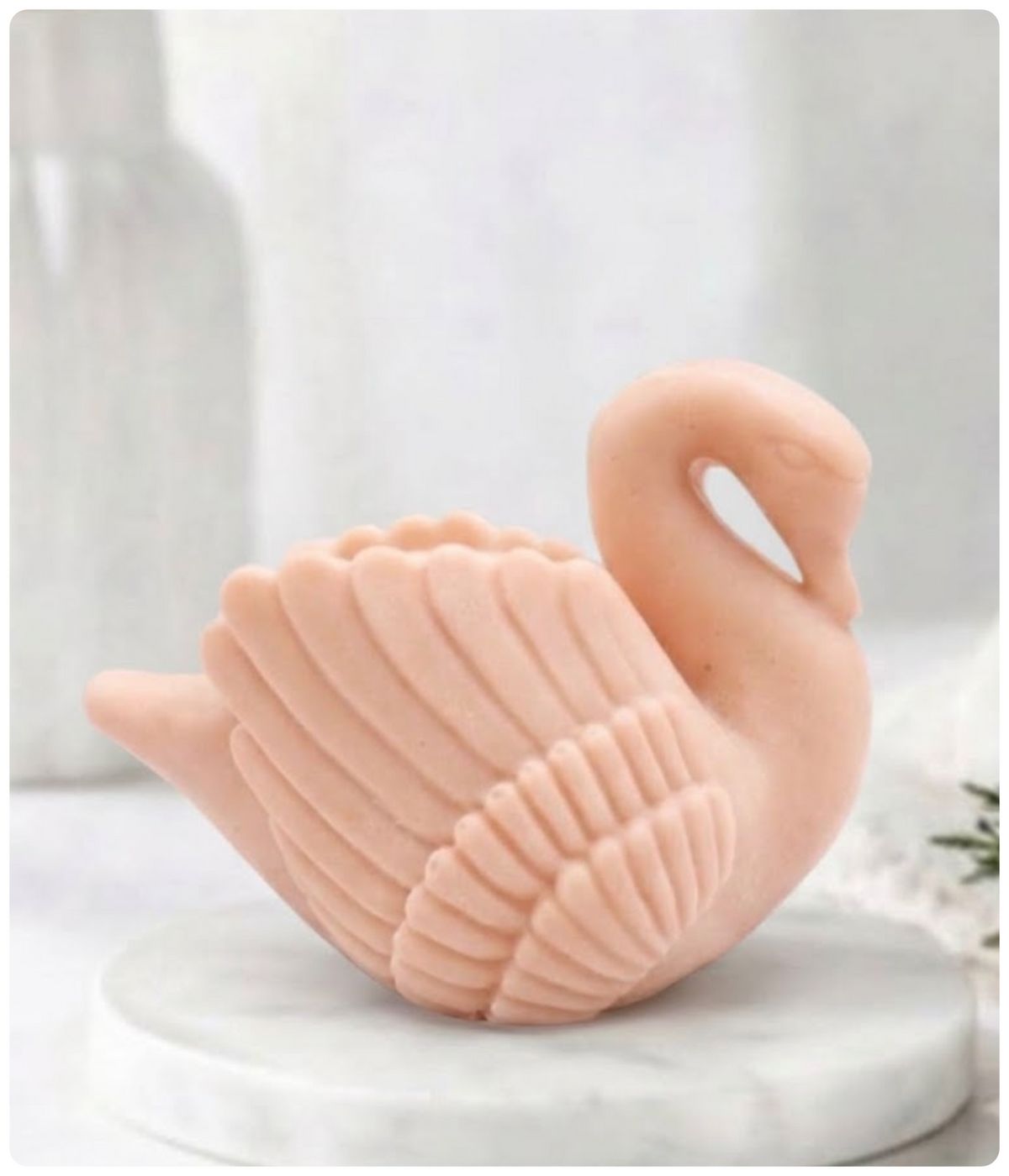 A side profile of a soft pink swan soap bar resting on a marble pedestal.