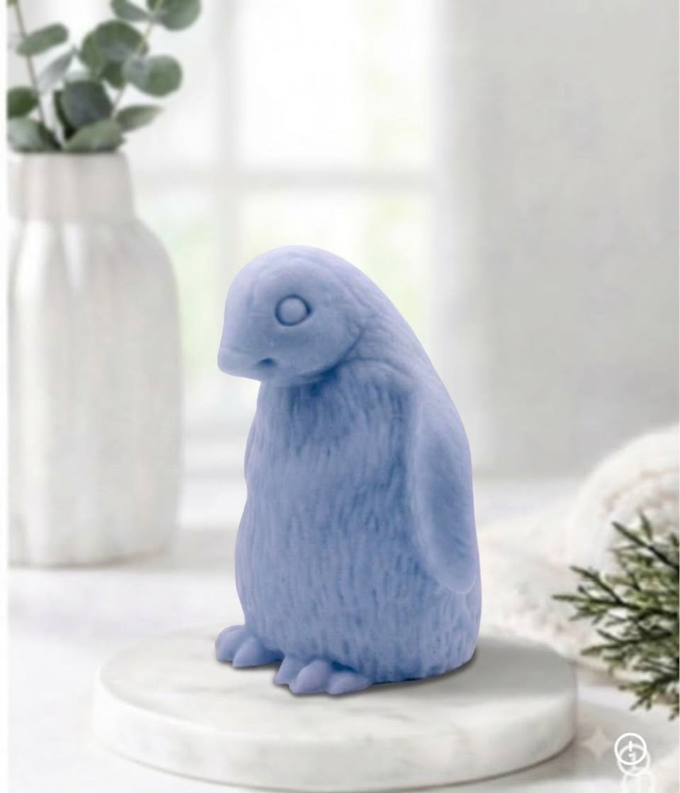 Handmade light blue indigo penguin-shaped soap bar displayed on a white marble tray.