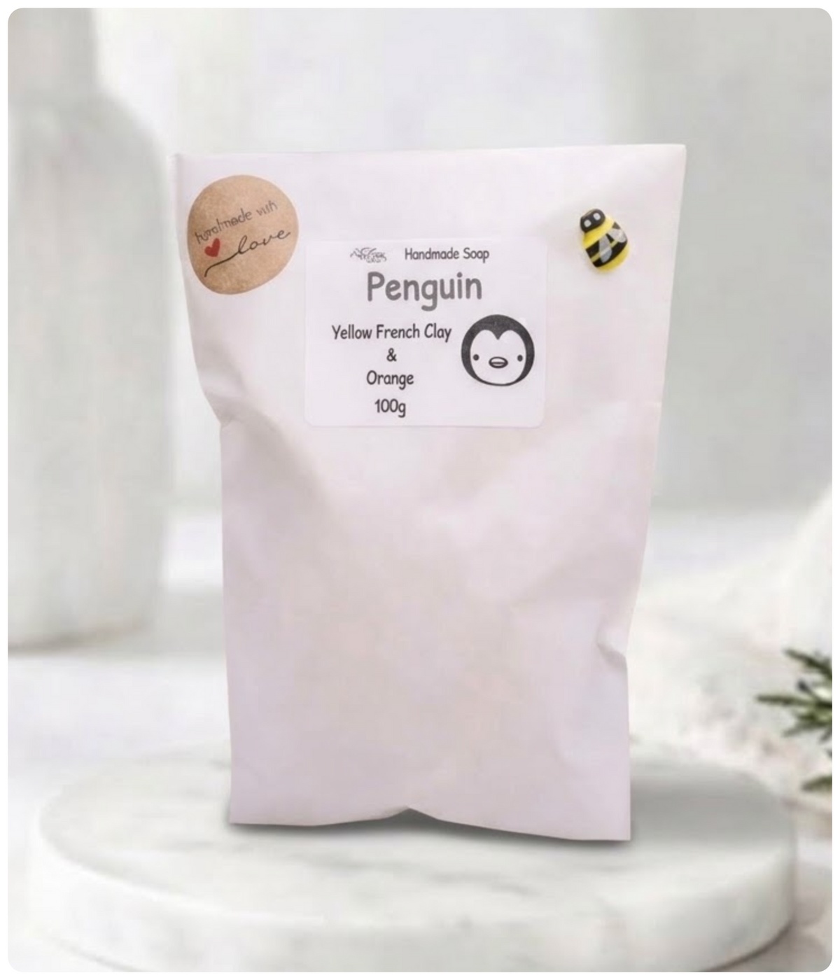 White paper eco-friendly soap packaging bag labeled "Penguin Handmade Soap" with a cute bumblebee accent craft pin.