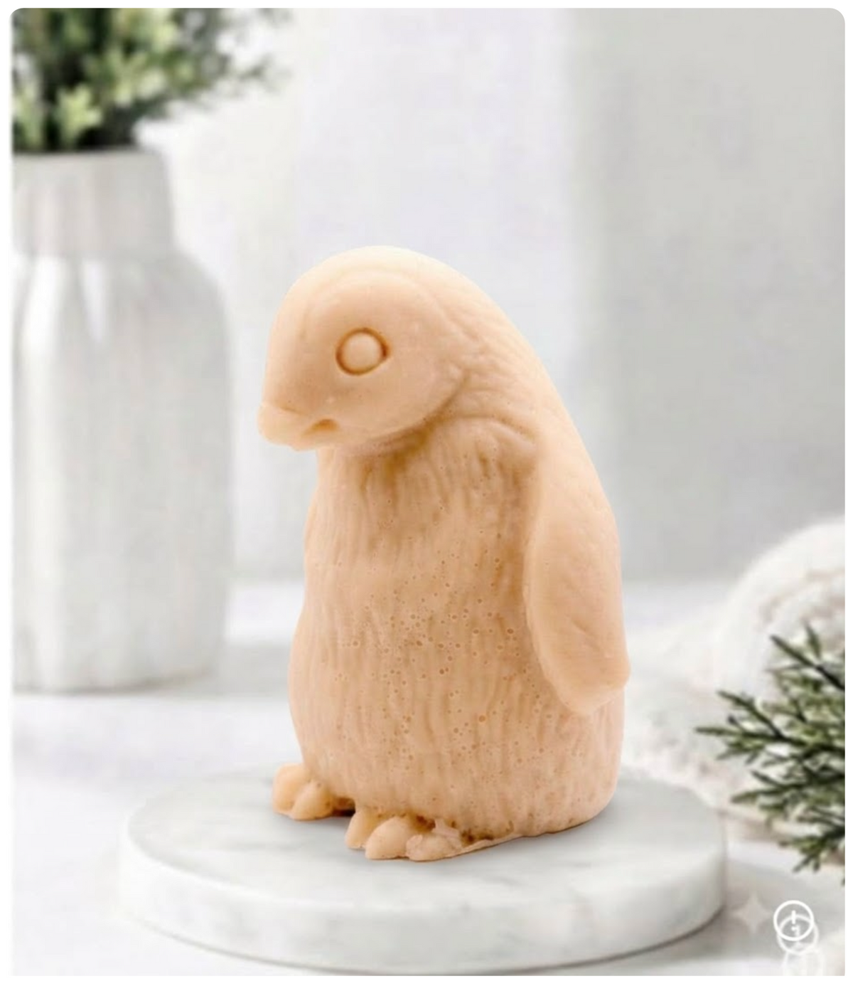 Handmade soft pink clay penguin-shaped soap sitting upright on a white marble display plate.
