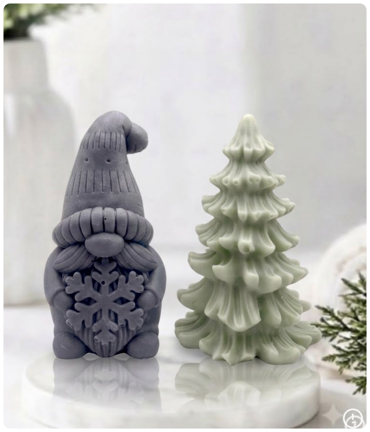 Charcoal grey gnome soap holding a snowflake next to a green pine tree soap on a marble tray.