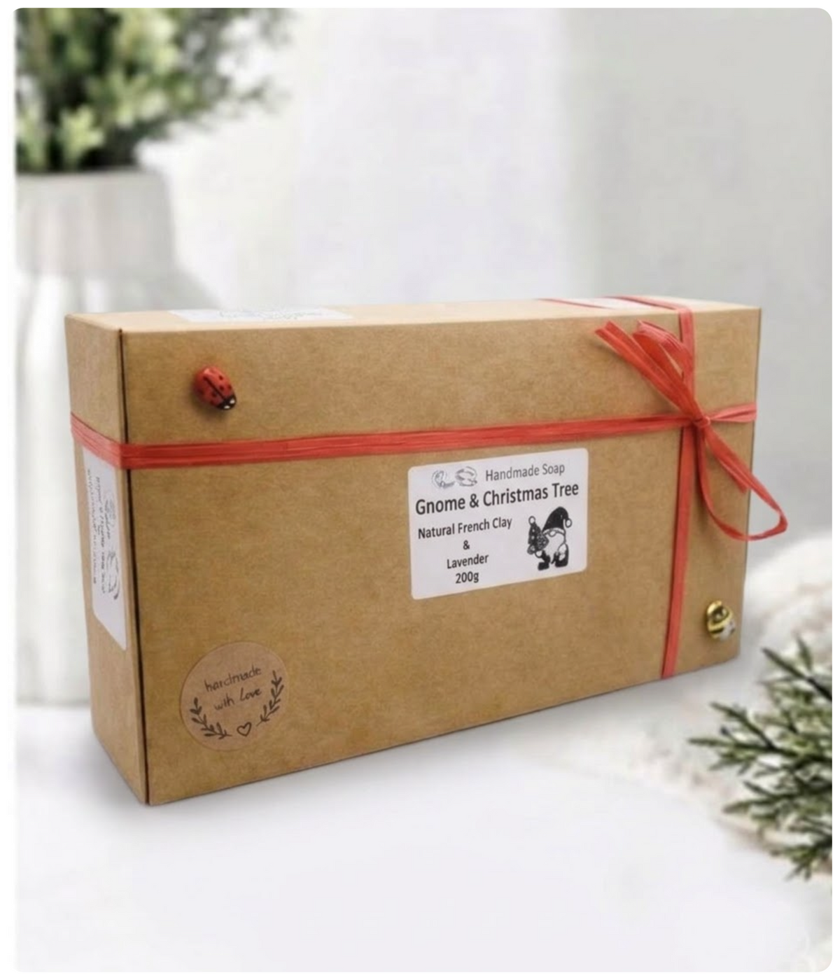 Cardboard gift box tied with red raffia ribbon and labeled "Gnome & Christmas Tree Handmade Soap”