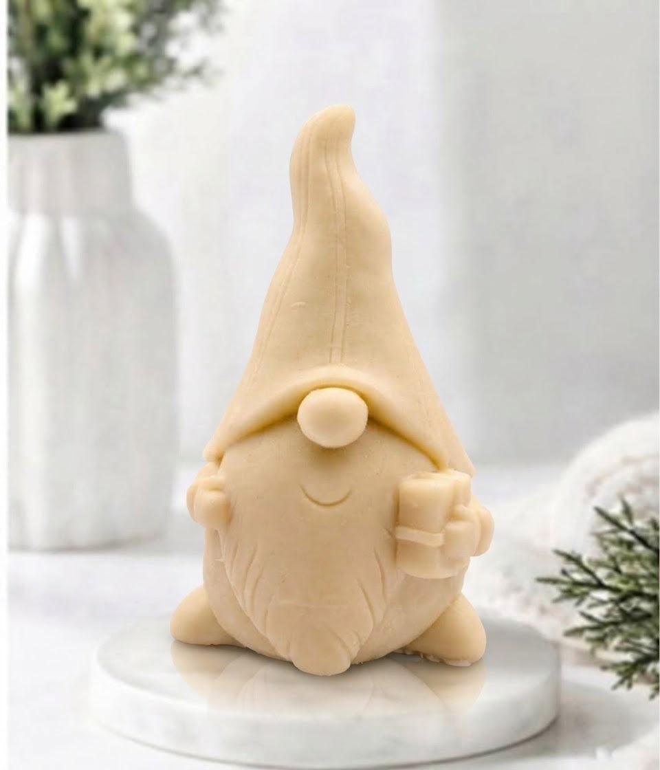 Front view of a yellow-coloured gnome-shaped soap bar holding a small gift box on a marble platter.