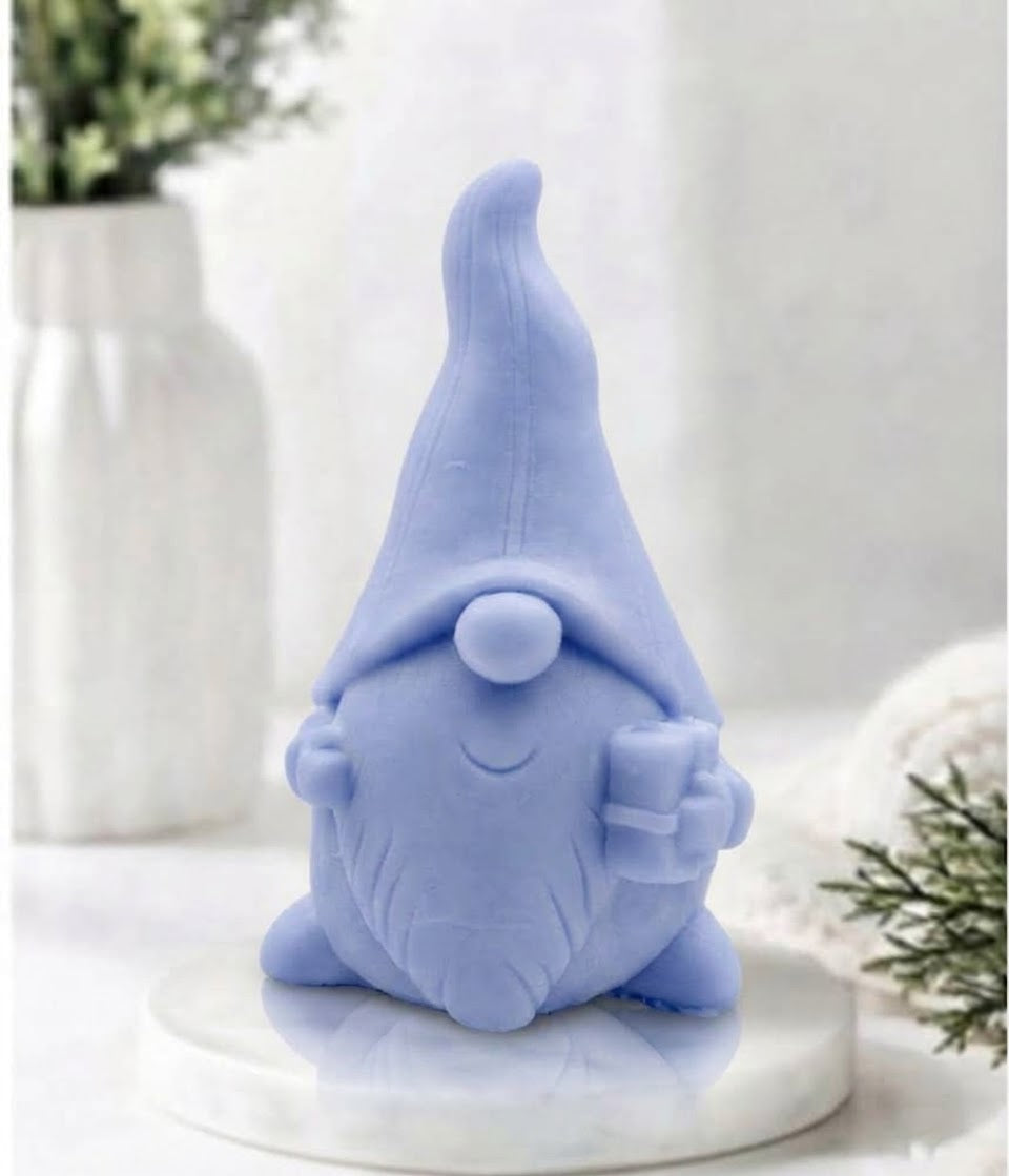 Front view of a pastel blue gnome-shaped soap bar holding a small gift box on a marble surface.