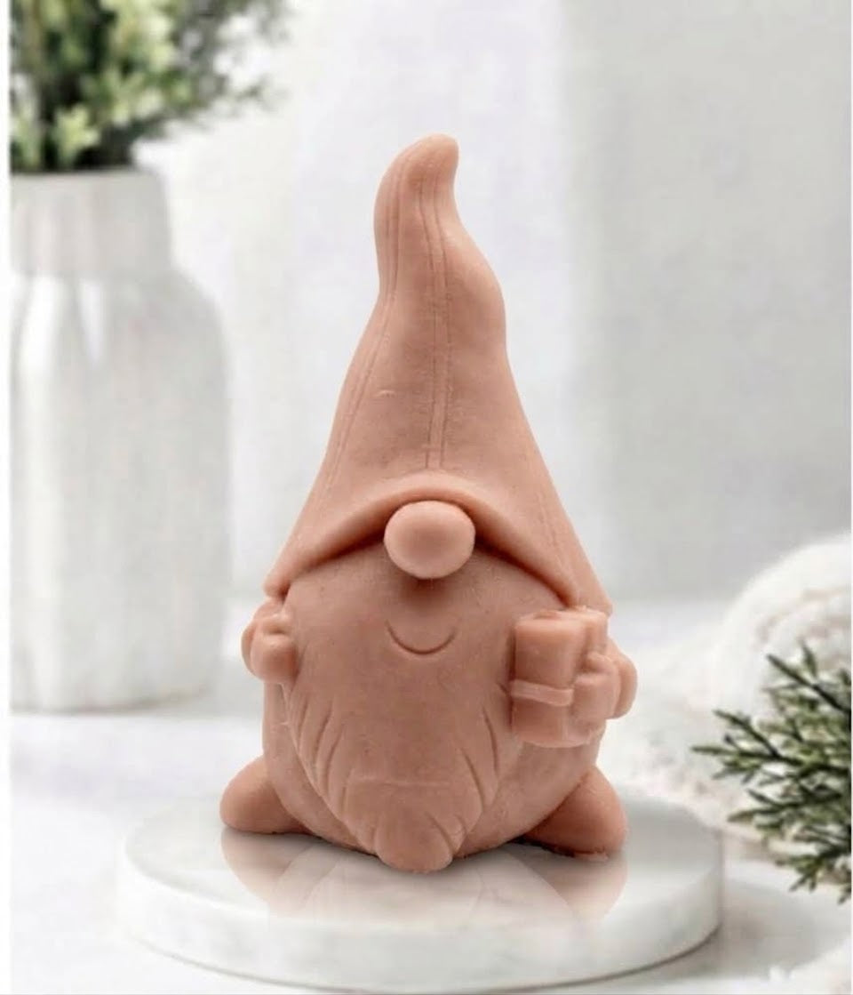 Front view of a red french clay gnome-shaped soap bar holding a small present on a marble display.