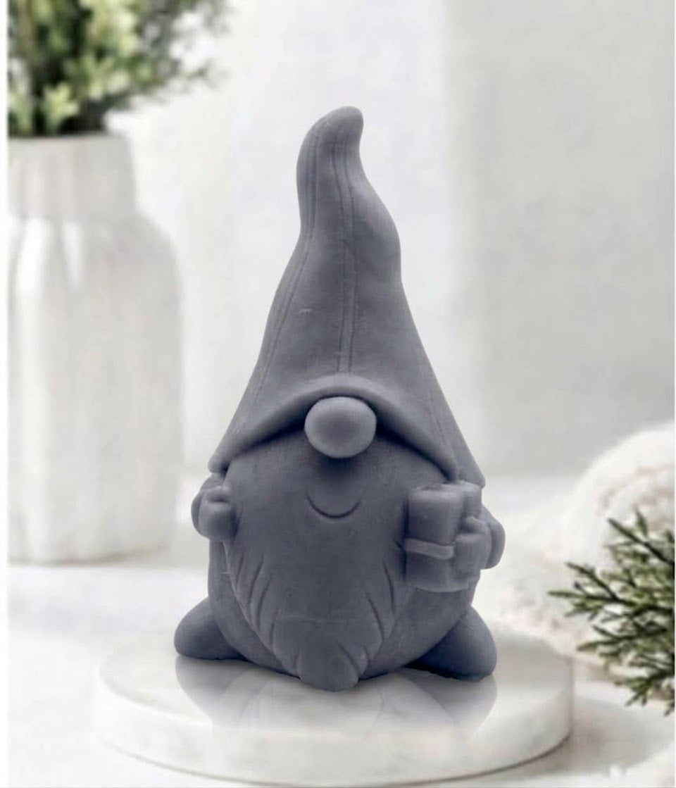 Front view of a charcoal grey gnome-shaped soap bar holding a small present on a marble surface.