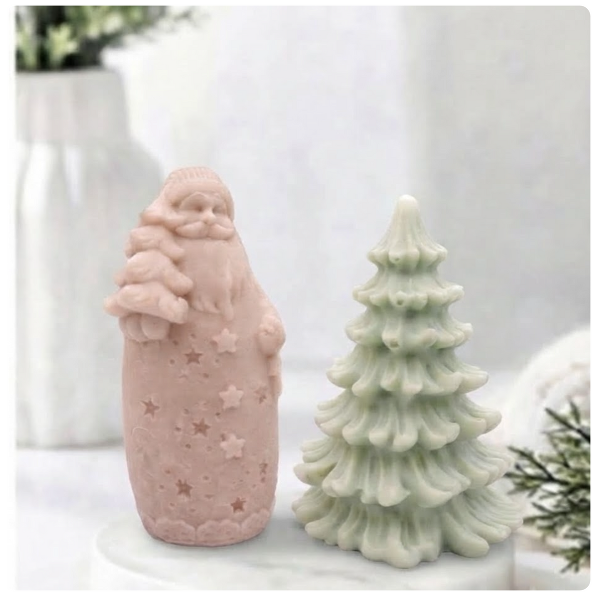 Pink Santa-shaped soap bar standing next to a green Christmas tree soap bar on a marble plate