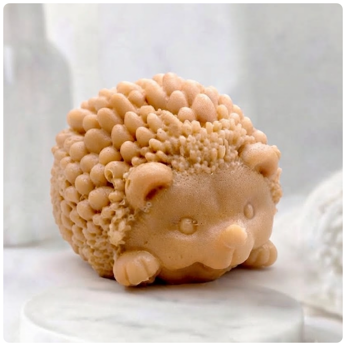 A terracotta , sculpted hedgehog soap figure, detailed with small spikes and a smiling face, sits on a white marble surface against a blurred bathroom background.
