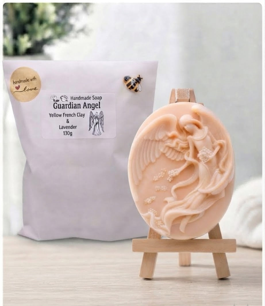 A pale pink Guardian Angel handcrafted soap bar displayed on a small wooden easel, with its white paper packaging pouch in the background.