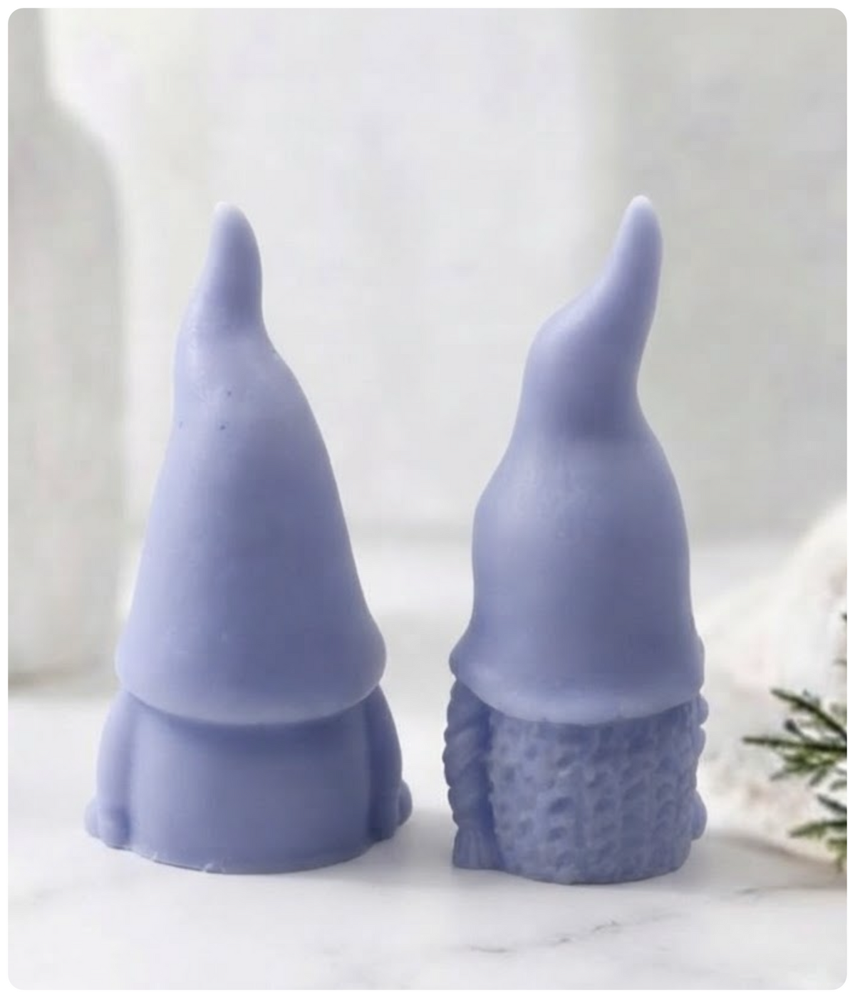 Two blue gnome-shaped soaps standing side by side on a light marble surface with a soft, blurred background.