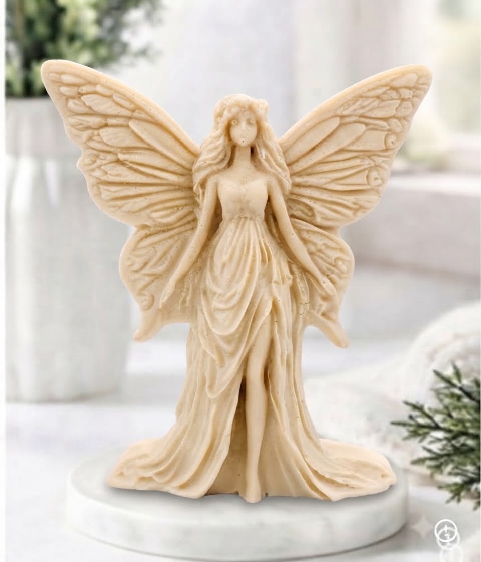 A yellow winged fairy vegan soap with detailed wings and a flowing gown, standing on a round white base against a softly blurred indoor background.