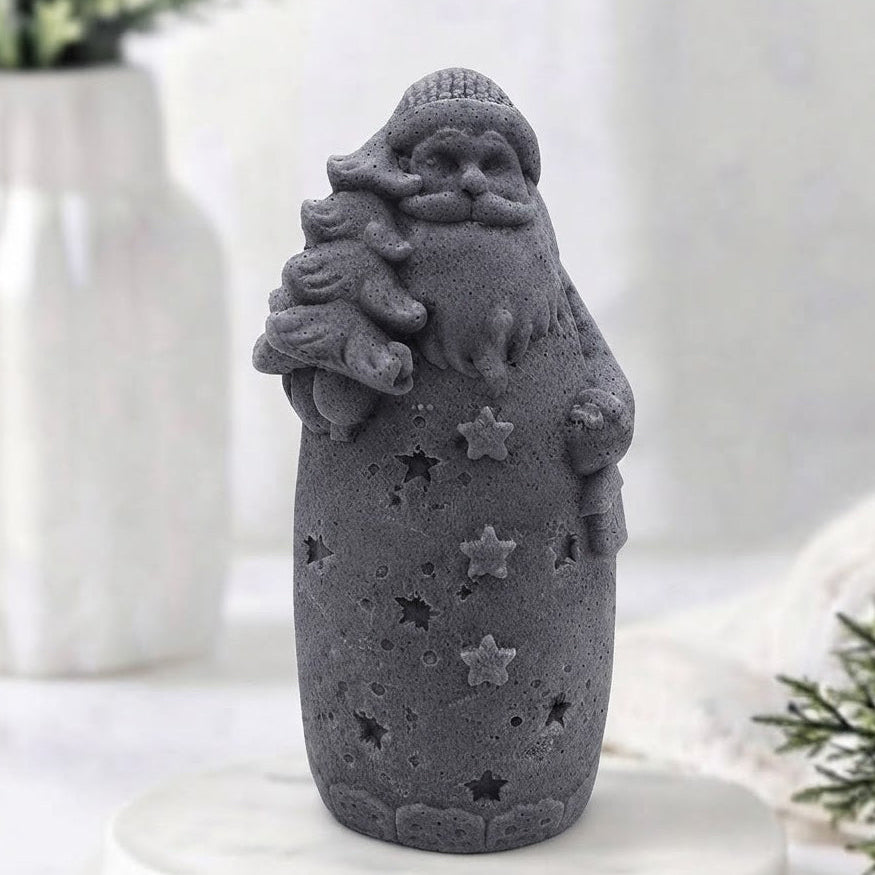 A charcoal grey Santa Claus vegan soap holding a Christmas tree, standing on a white marble round tray with a softly blurred indoor background.
