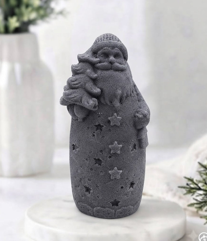 A charcoal grey Santa Claus vegan soap holding a Christmas tree, standing on a white marble round tray with a softly blurred indoor background.