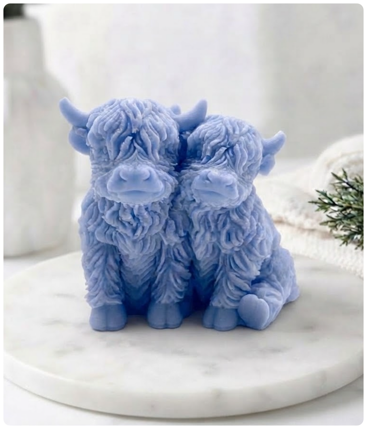 Two blue Highland cow vegan soaps sitting together on a round white marble tray, with a softly blurred indoor background.