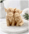 Two yellow Highland cow vegan soaps with textured fur, sitting side by side on a round white marble platter against a softly blurred background.
