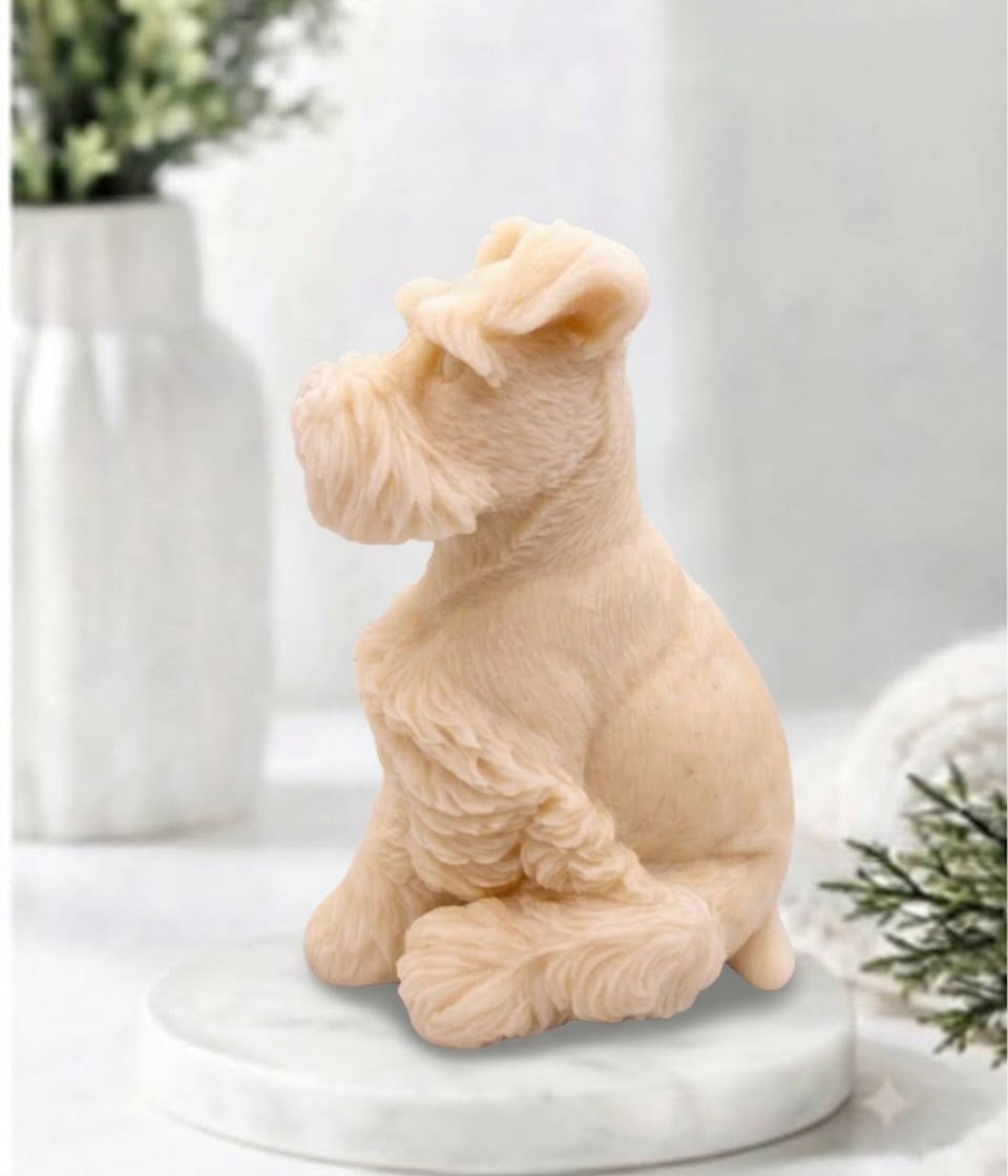 A soft pink schnauzer dog figurine, shaped like a Schnauzer, sitting on a round white marble base. The background is a soft-focus white setting with a white vase containing green leaves.
