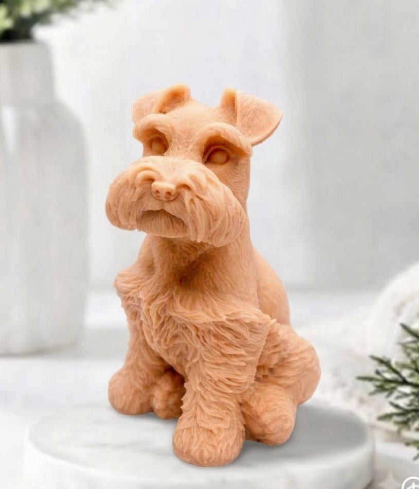A terracotta coloured schnauzer dog vegan soap, posed sitting on a round white marble plinth with a softly blurred indoor background and decorative plants.
