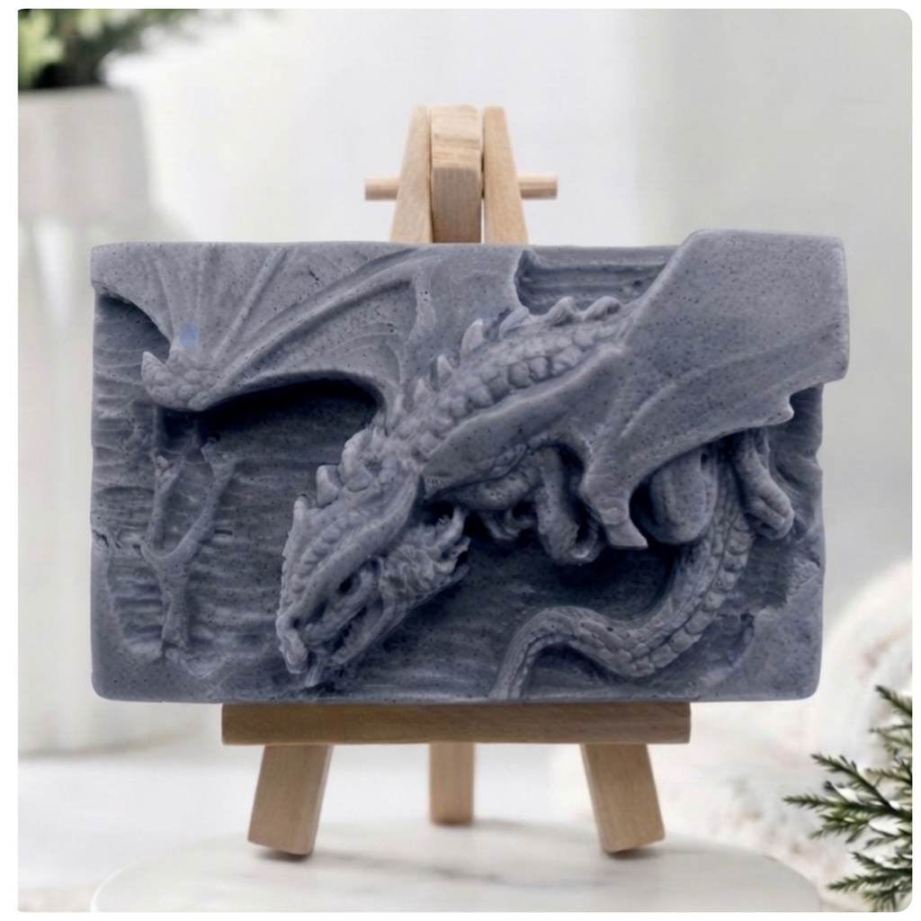 A gray rectangular relief vegan soap featuring a detailed dragon carving, displayed on a small wooden easel against a softly blurred indoor background.