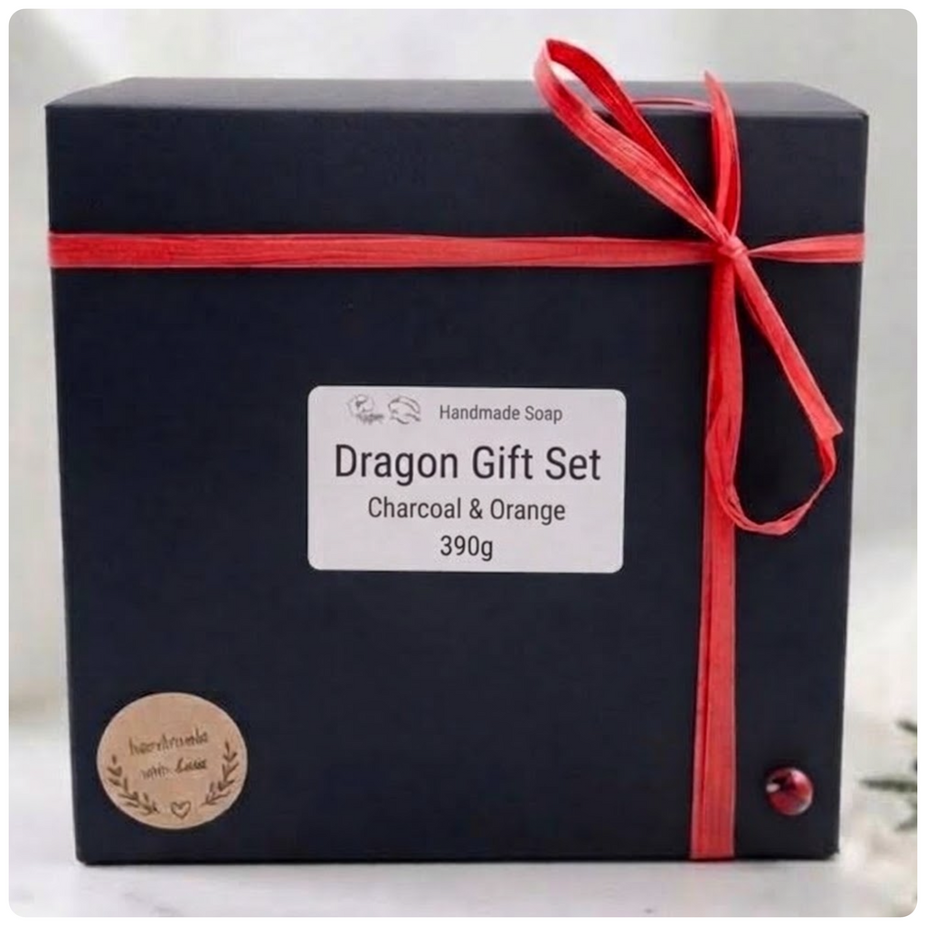A black rectangular gift box for handmade soap, tied with a red ribbon and bow. A white label on the front reads 'Dragon Gift Set', 'Charcoal & Orange', and '390g'.