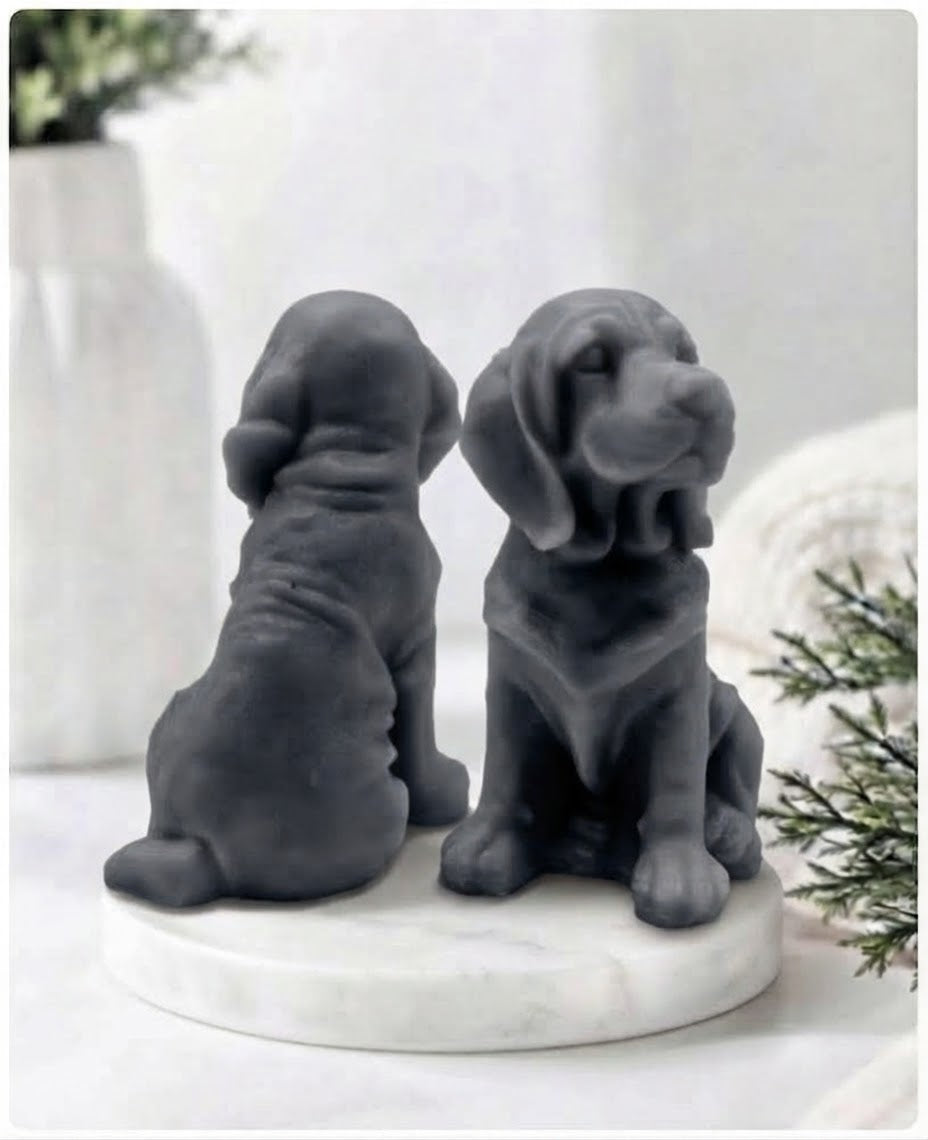 Two charcoal grey bloodhound soap sitting on a white marble display stand with a soft bathroom background.