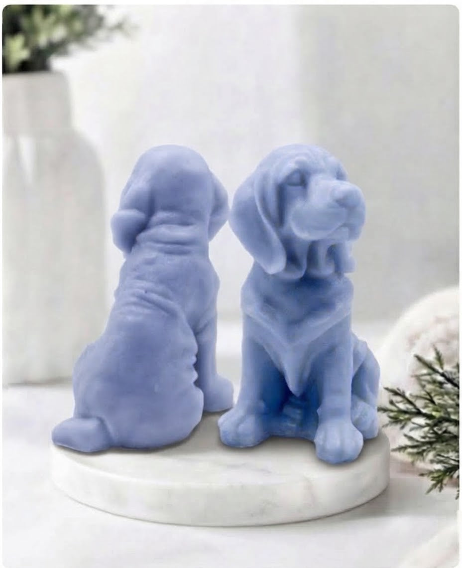 Two indigo blue bloodhound soaps sitting on a white marble display stand with a soft bathroom background.